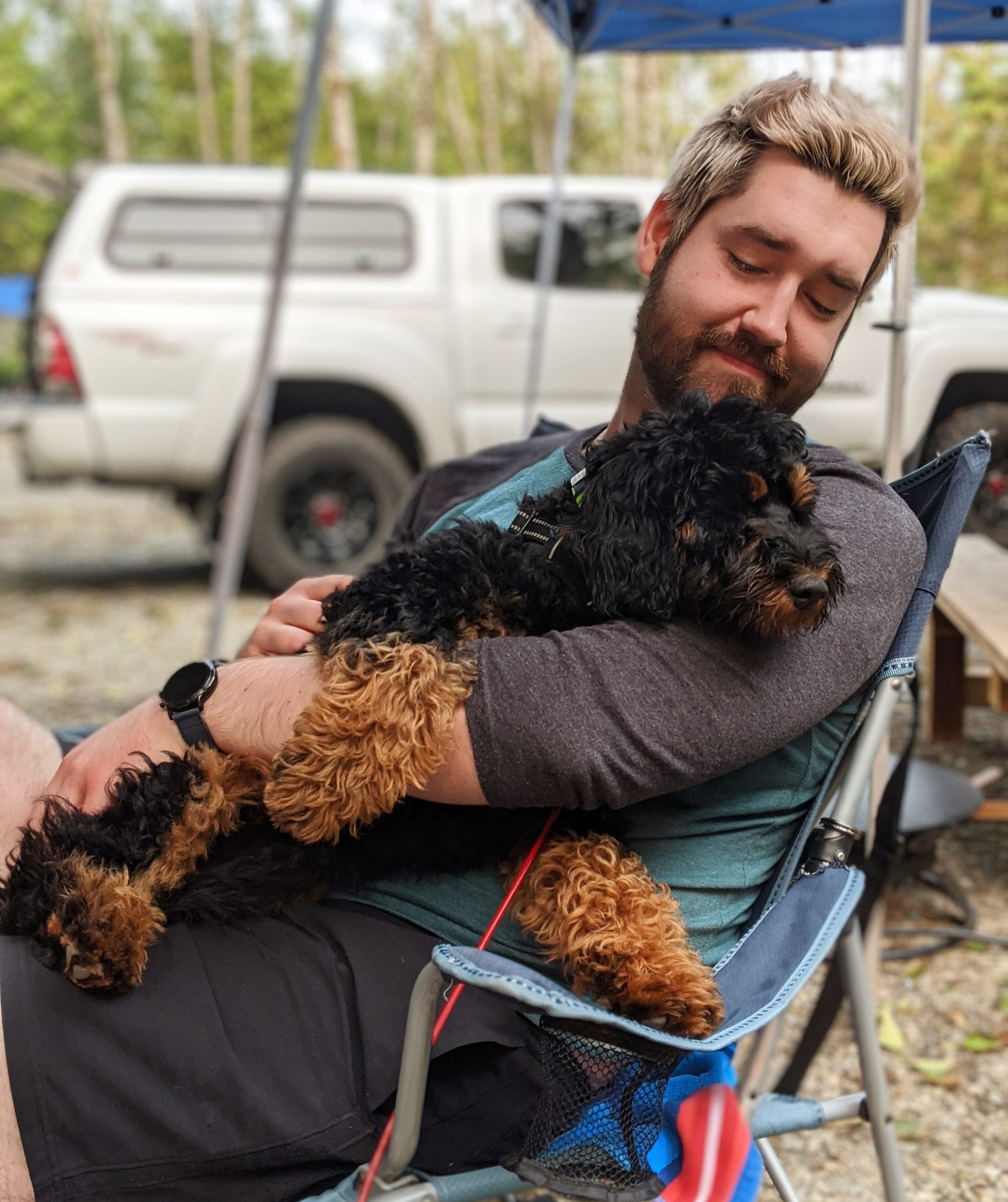 Registered Clinical Counsellor, Mark Antczak on a camping trip, sitting in a camp chair snuggling his dog, Maslow