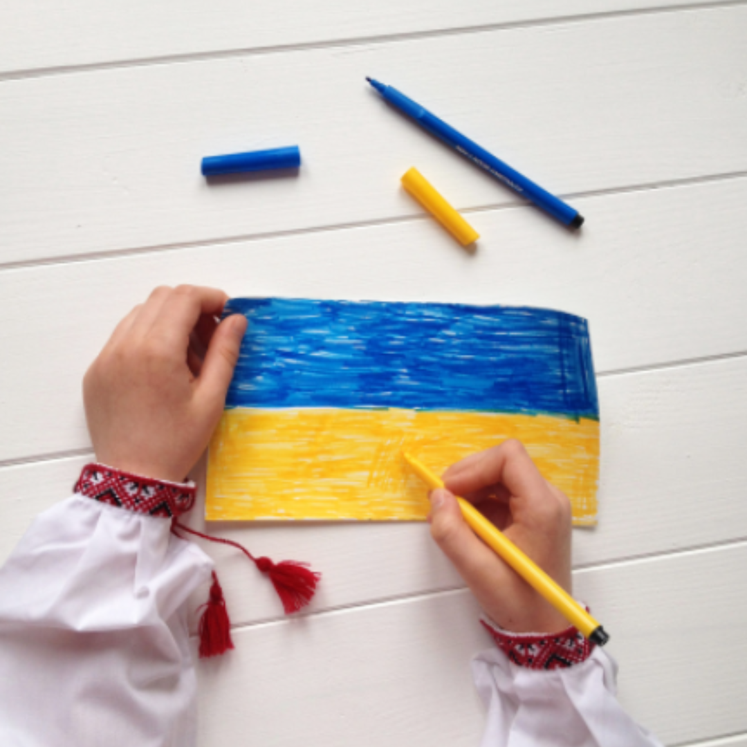 Child drawing a Ukraine flag with coloured pencils