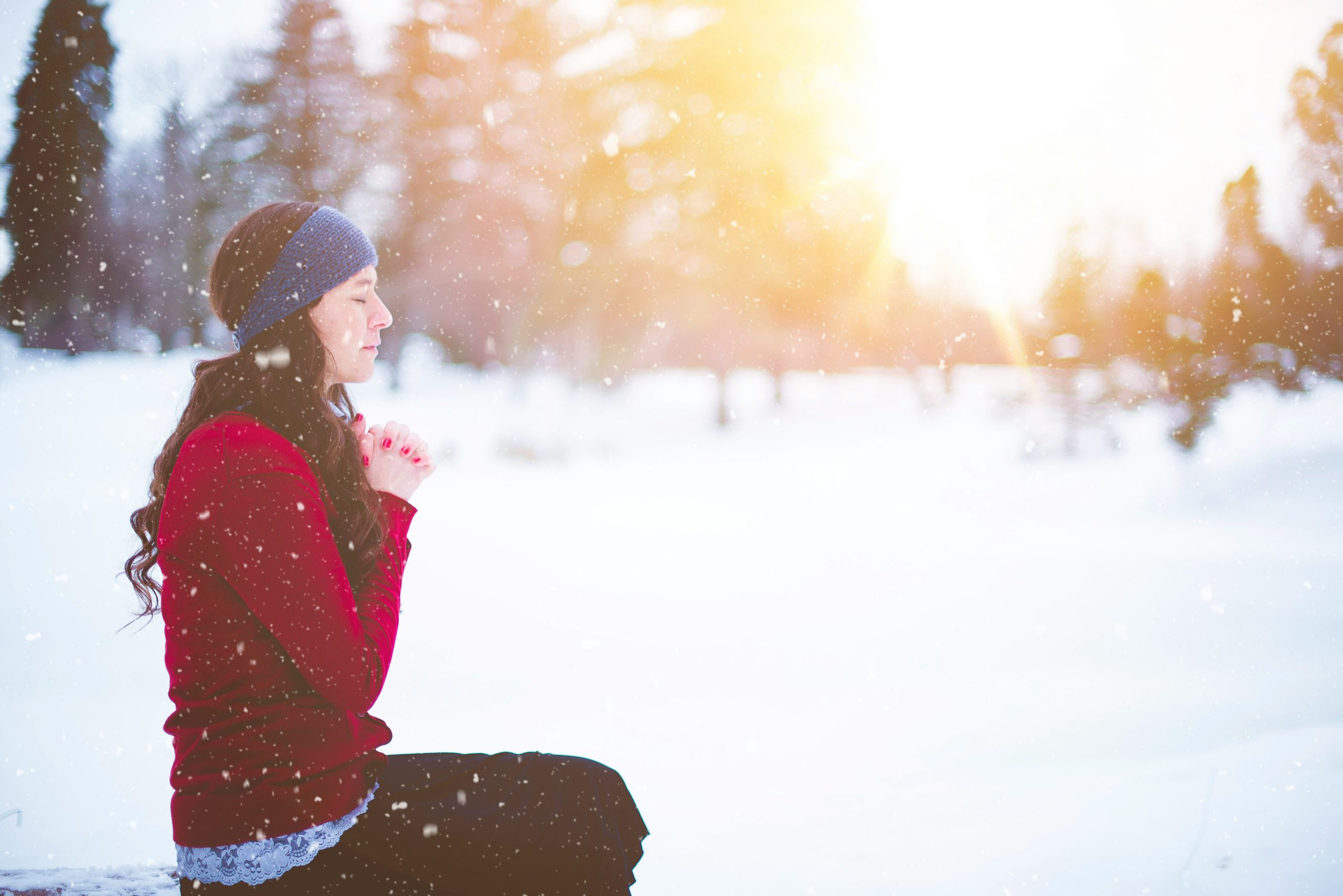 woman sitting in the snow with eyes closed and hands clasped together